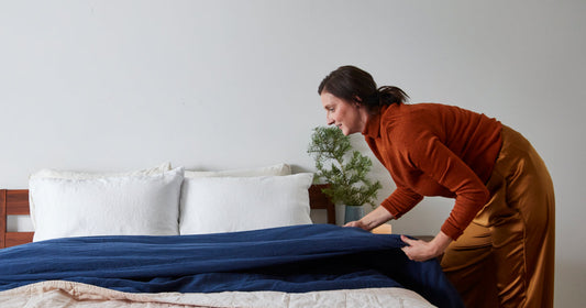 Woman folding a blue blanket on top of her already made bed.
