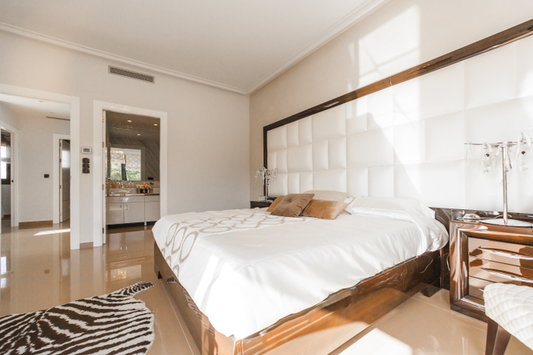 Picture of a bedroom with a zebra rug on the floor, bed made in white bedding and a white puffy headboard outlined in wood that takes up most of the wall