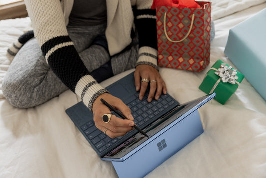 Arial view of someone sitting on a bed with a few wrapped gifts next to them while they look on a laptop