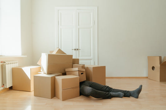 Man laying on the floor under a pile of boxes. All you can see are the stack of boxes and his legs.