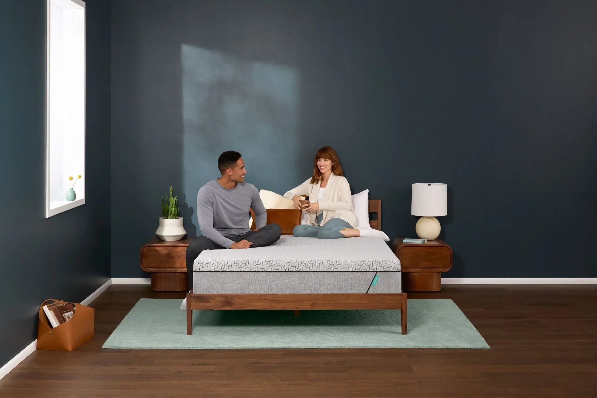 Man laying on the left and woman sitting on the right of a Tuft and Needle Original Hybrid mattress