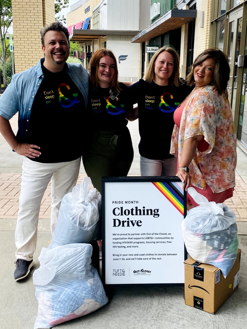 T&N employees taking a group photo wearing pride tees in front of the clothing drive pride month sign