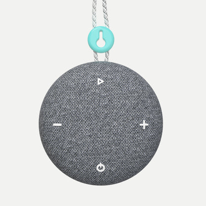 A Tuft and Needle SNOOZ Go 2 Travel White Noise Sound Machine, round gray fabric-covered speaker with white control icons on the front, hanging from a white rope with a turquoise accent ring.