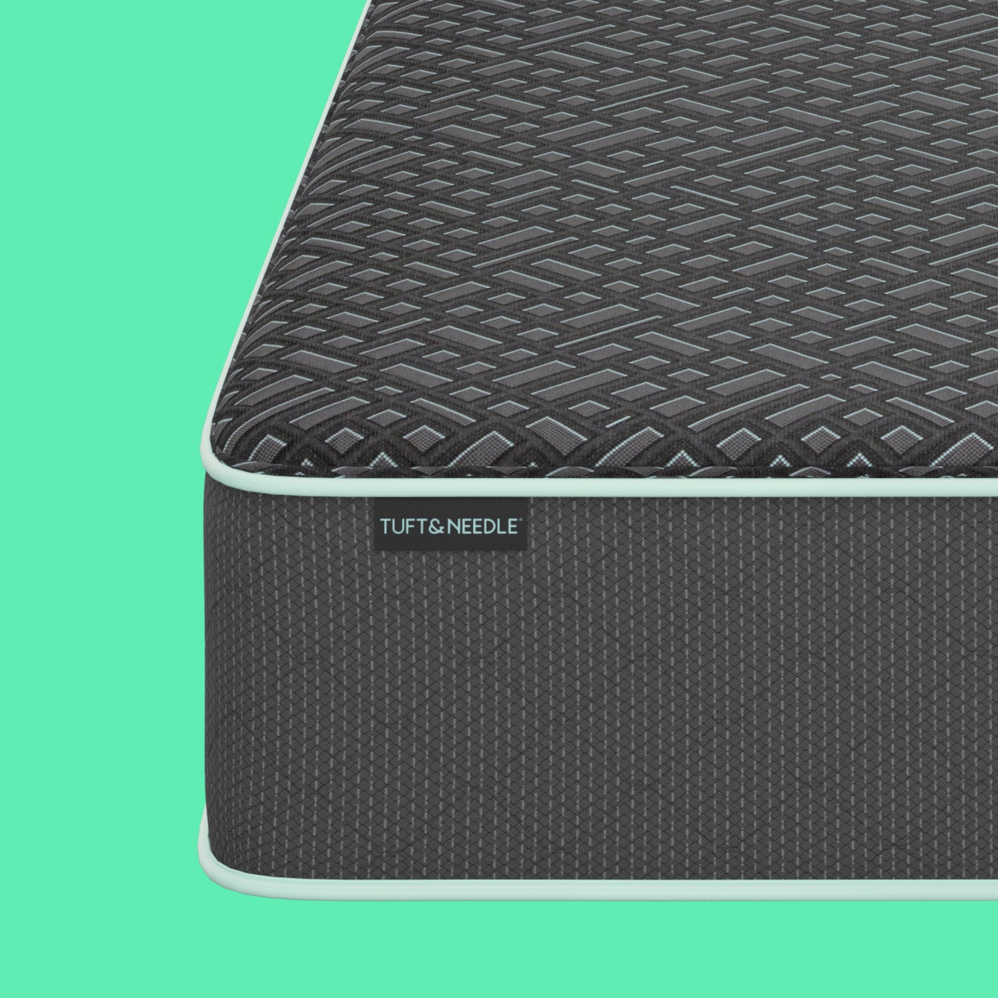 A dark gray Tuft & Needle textured mattress shown at an angle against a mint green background with abstract light green shapes. The brand name Tuft & Needle is visible on a small label on the side of the mattress.