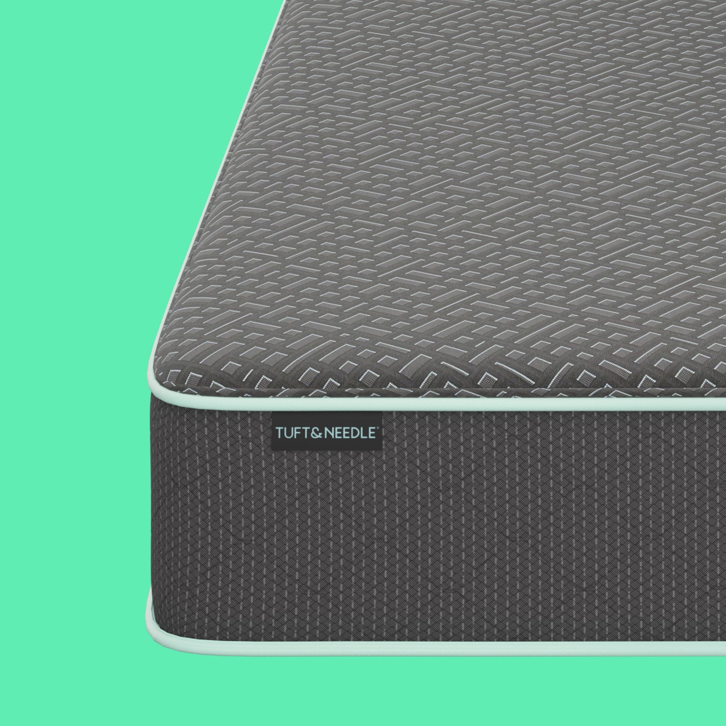 Close-up of a Tuft and Needle mattress corner showing a textured gray top surface and dark gray side panel with a visible TUFT & NEEDLE brand tag, set against a solid mint green background.