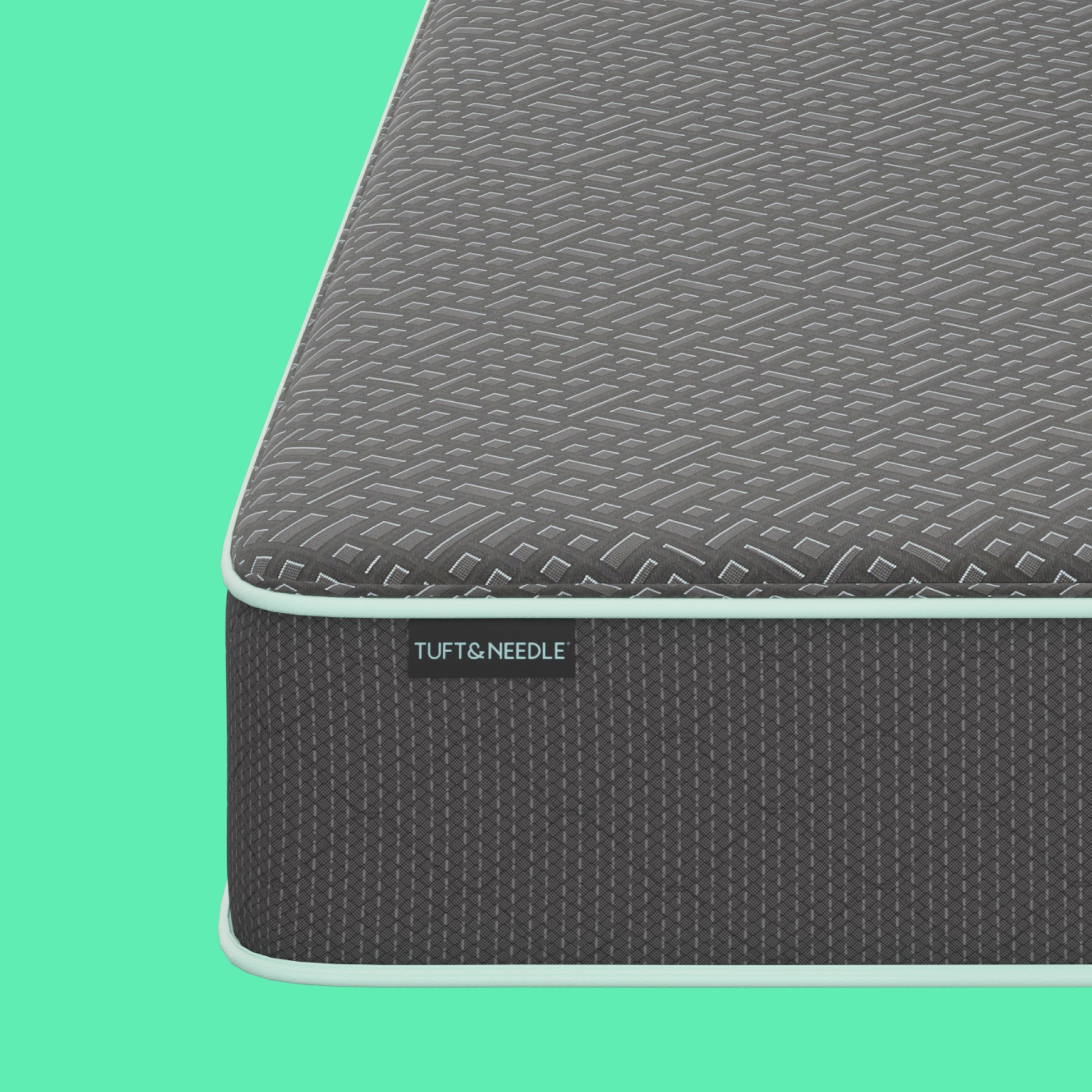 Close-up of a Tuft and Needle mattress corner showing a textured gray top surface and dark gray side panel with a visible TUFT & NEEDLE brand tag, set against a solid mint green background.