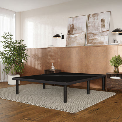 A black Baselogic Platform with four legs, set on a textured beige rug in a modern room with wood floors, a copper-colored accent wall, and abstract wall art.