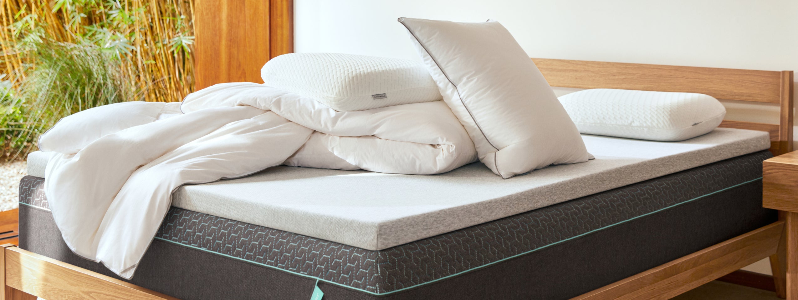 Tuft & Needle bedding, 3 white pillows and a white comforter, and a grey mattress topper on top of a Tuft and Needle Mint mattress in a Brown bed frame