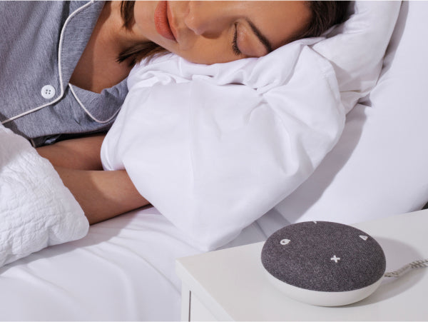 Woman laying asleep on her left side asleep on on a tuft and needle mattress with a Snooz Go Travel White Noise Machine to the left on a night stand.