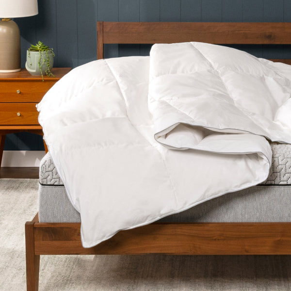 White Tuft & Needle comforter on a wooden bed with a nightstand and lamp in the background.