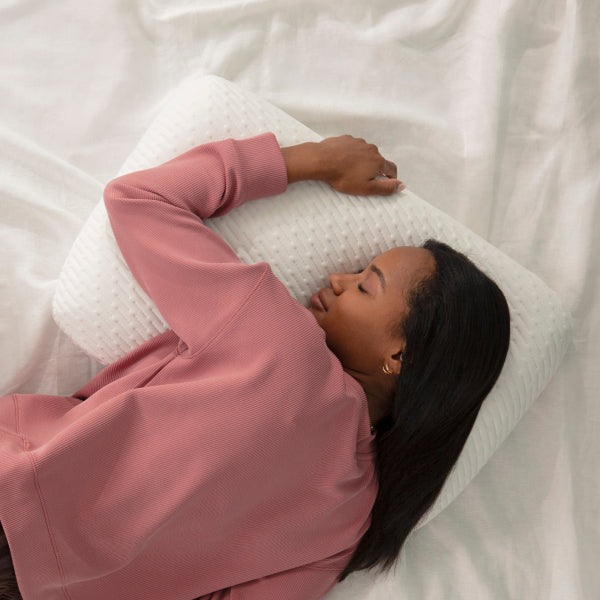 Woman wearing a pink sweatshirt lying on a Tuft and Needle white pillow on top of a Tuft and Needle mattress