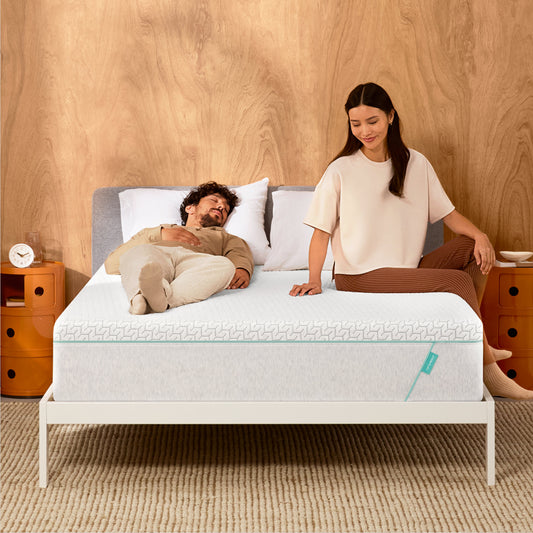 Man and woman laying on a Tuft & Needle Original Hybrid mattress sitting in a white bedframe