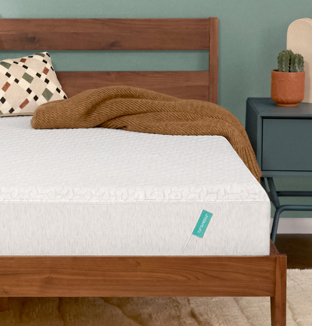 Tuft & Needle Original mattress on a wooden bed frame with a brown blanket and patterned pillow.