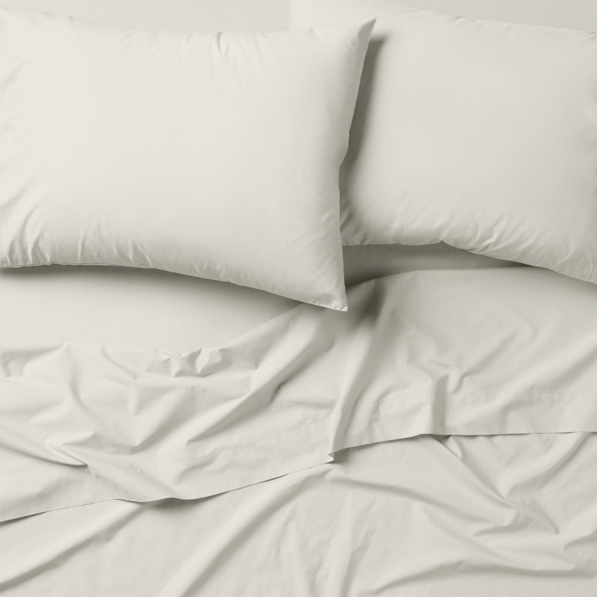 The Tuft and Needle Classic Percale Sheet Set, 2 pillows on top of a sheet on a mattress || color: Sage
