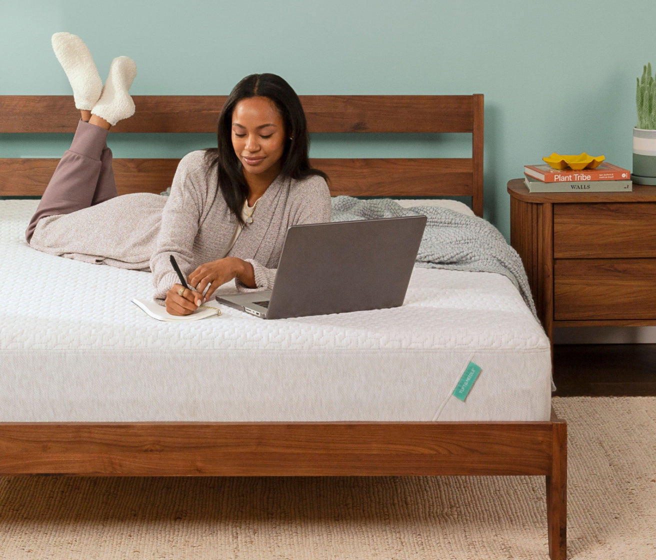 Woman laying on a Tuft and Needle Original mattress writing on a notepad in front of her laptop