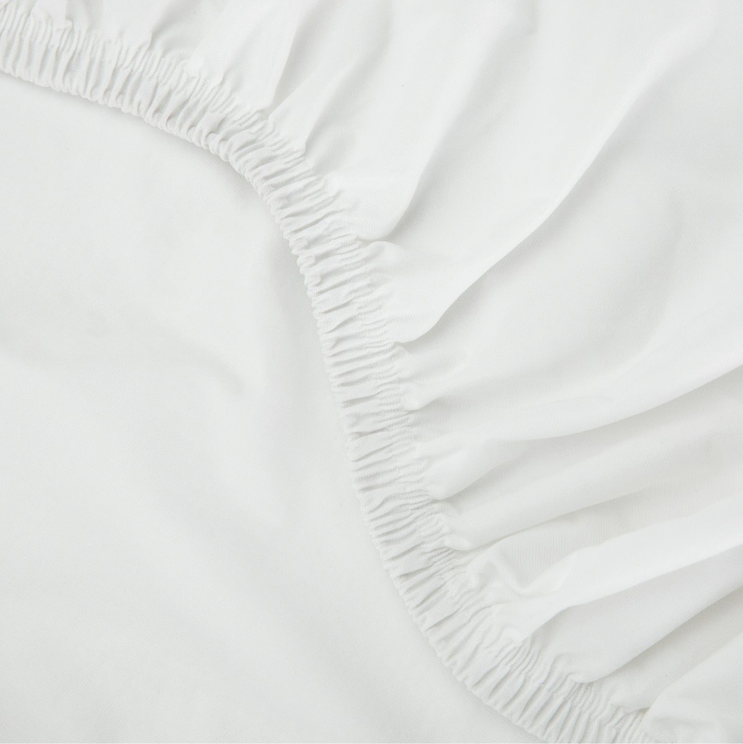  Close-up of a Tuft & Needle white fitted sheet with elastic waistband on a bed.