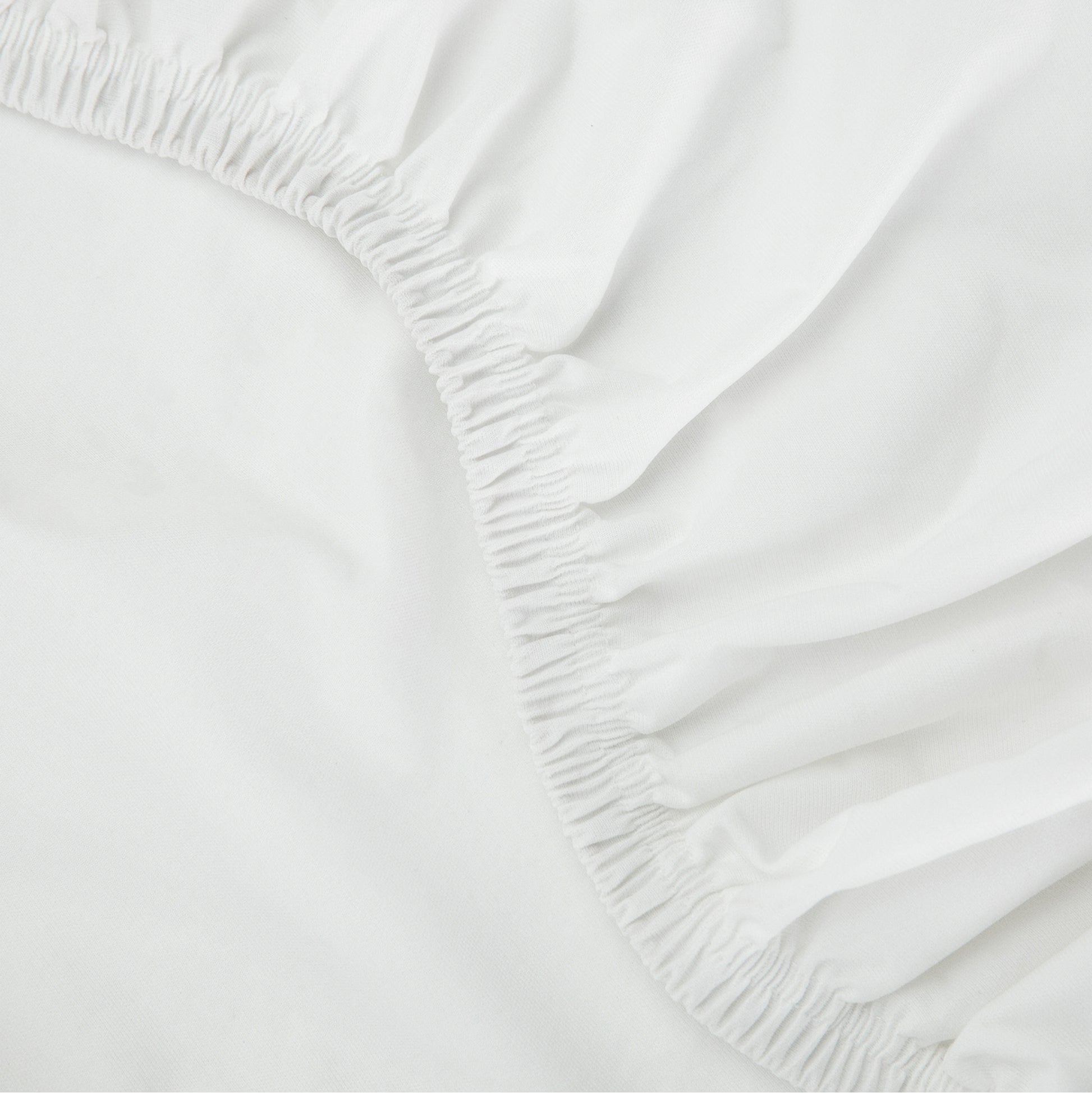  Close-up of a Tuft & Needle white fitted sheet with elastic waistband on a bed.