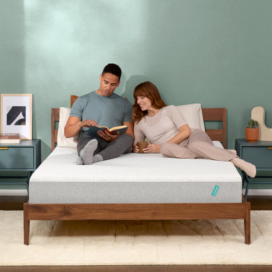 A couple relaxes on a modern bed with a light grey mattress, reading and drinking coffee in a cozy, minimalist bedroom.